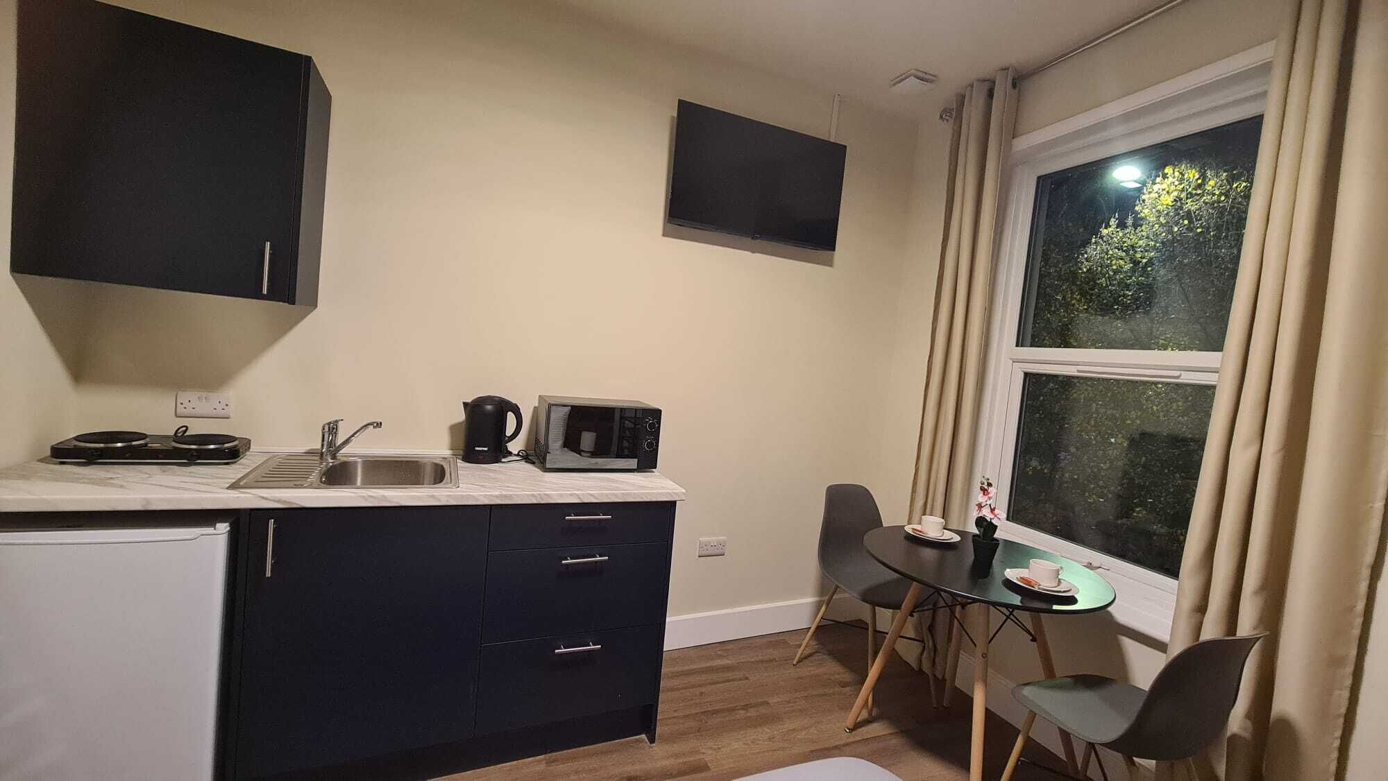 A compact kitchen with a sink, kettle, microwave, and a small dining table with chairs.