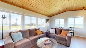 Ein geräumiges Wohnzimmer mit zwei Sofas, einem Glastisch und großen Fenstern mit Blick auf den Strand.