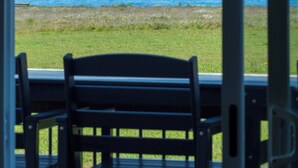 Blick auf das Meer durch ein Fenster, im Vordergrund eine Rasenfläche und eine Bank.