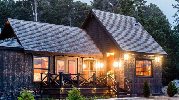 Eine rustikale Holzhütte mit einer Veranda, Sitzgelegenheiten und einem Schornstein.