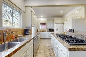 Una cocina moderna con armarios blancos, encimeras de granito, un lavamanos de acero inoxidable, un microondas, una estufa y un refrigerador.