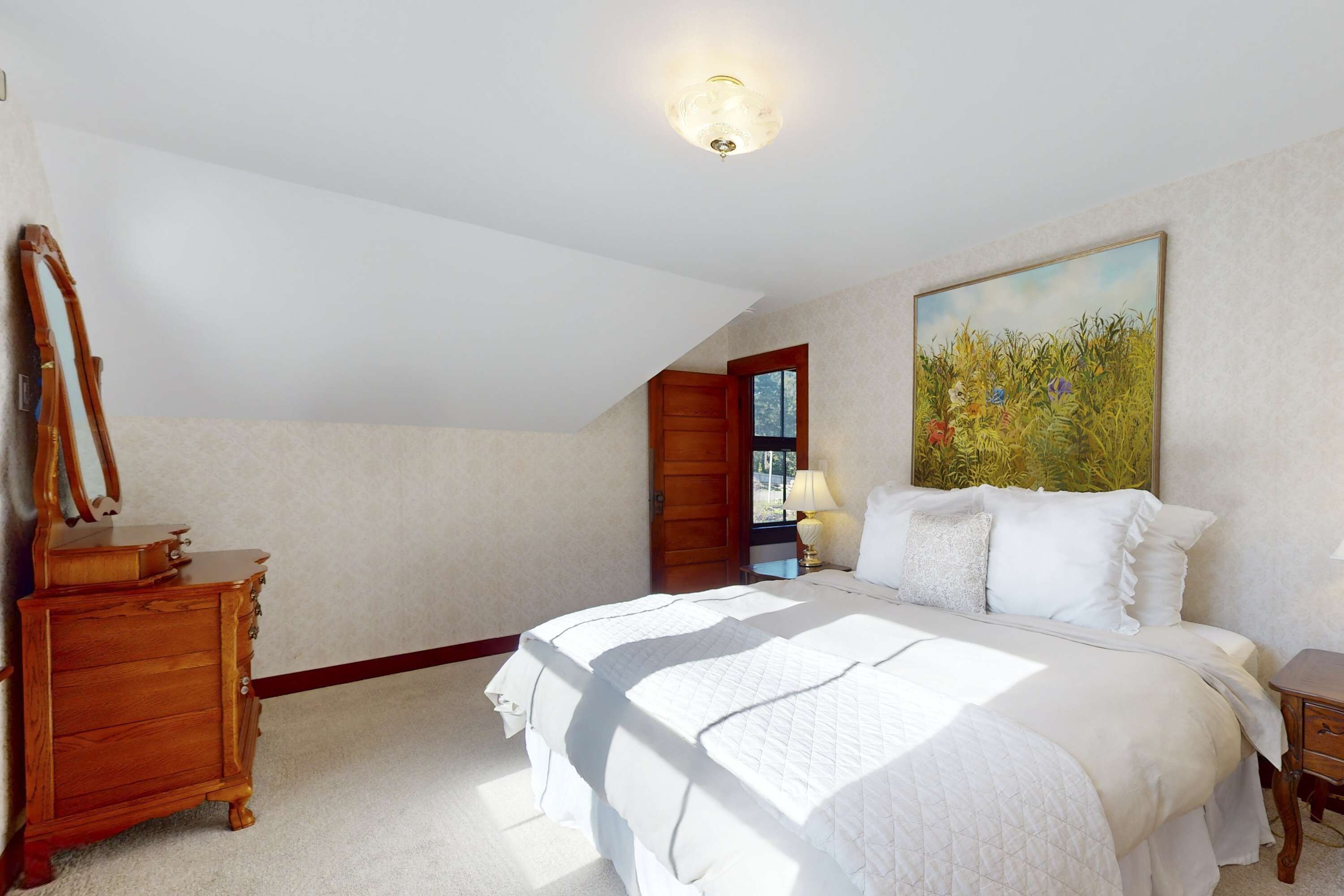 A bedroom with a large bed, a dresser, a mirror, and a painting on the wall.