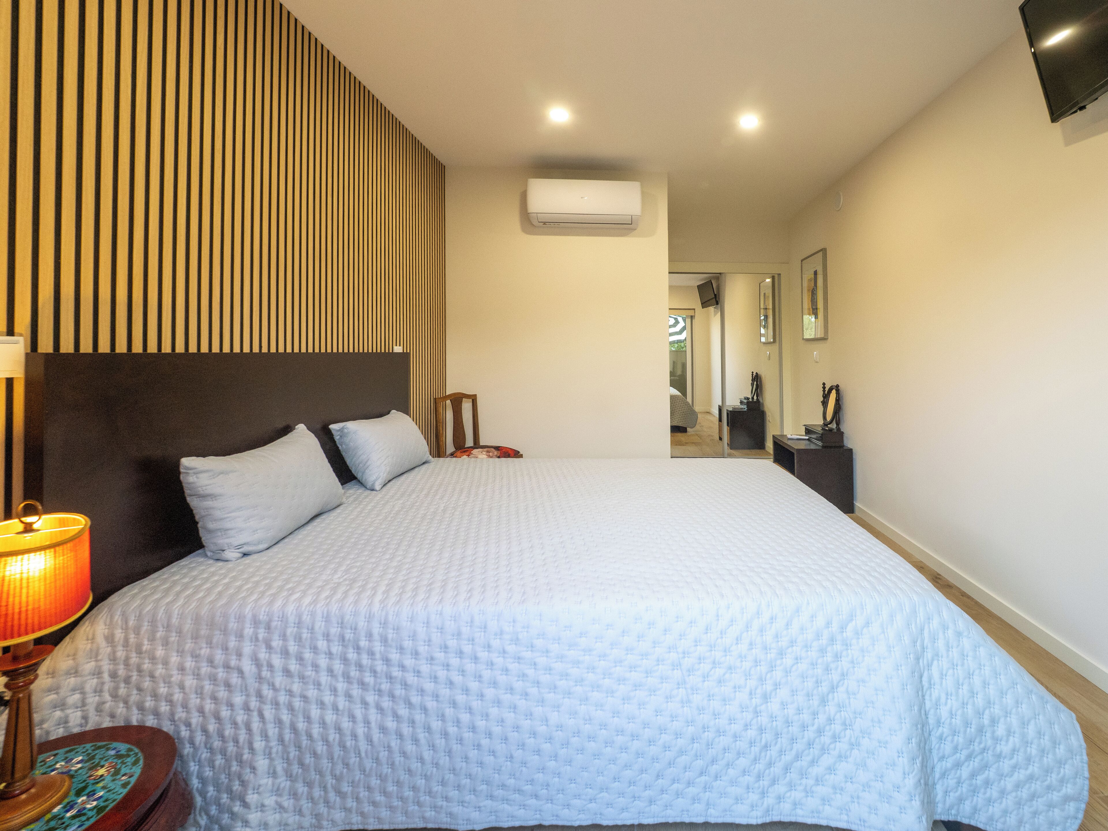 Une chambre d’hôtel avec un grand lit, une lampe de chevet, un téléviseur à écran plat et un miroir au mur.