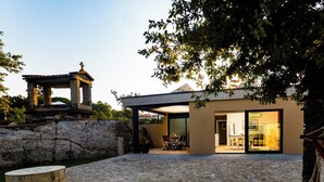 Une cour pavée de pierres avec un belvédère, un bâtiment moderne doté d’une porte en verre et un arbre.