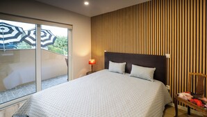 Une chambre moderne avec un grand lit, un mur lambrissé en bois, une petite table de chevet et une vue sur l’extérieur grâce à une porte vitrée.