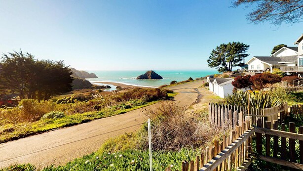 Eine Küstenstraße mit Holzlattenzaun, Strand und Häusern mit Meerblick.