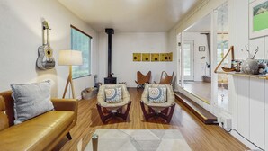 Una sala de estar con un sofá de cuero marrón, dos sillones con cojines estampados, una guitarra, una lámpara y una chimenea.