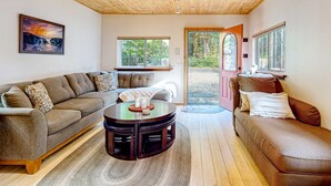Una sala de estar acogedora con techo de madera, un sofá, una mesa de centro y un ventanal con vistas al verdor.