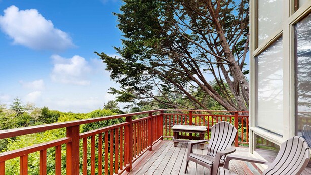 Une terrasse en bois avec une rambarde rouge, deux fauteuils Adirondack et une petite table.