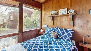 Une chambre à coucher située dans une cabane en bois, avec un grand lit, des poutres apparentes, une fenêtre et une étagère ornée d’objets décoratifs.