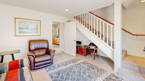 Ein Wohnzimmer mit braunem Ledersessel, einem gemusterten Teppich, einem gerahmten Bild an der Wand und einer Treppe mit weißen Gel ändern.