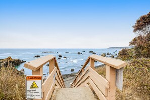Eine Holztreppe führt zu einem Strand, mit einem Warnschild wegen hoher Wellen.