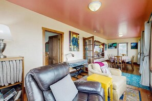 A living room with a leather sofa, a yellow side table, a dining area with a table and chairs, and a bookshelf.