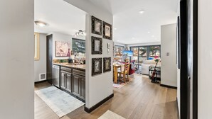 Eine moderne Küche mit Edelstahlgeräten, ein Essbereich mit Holztisch und -stühlen sowie ein Wohnzimmer mit großem Fenster.