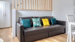 A modern living room with a dark brown leather sofa, four colorful cushions, a wooden slatted ceiling, and a white chair. - Blue Bird, charmant studio avec place de parking ! (Rouen)