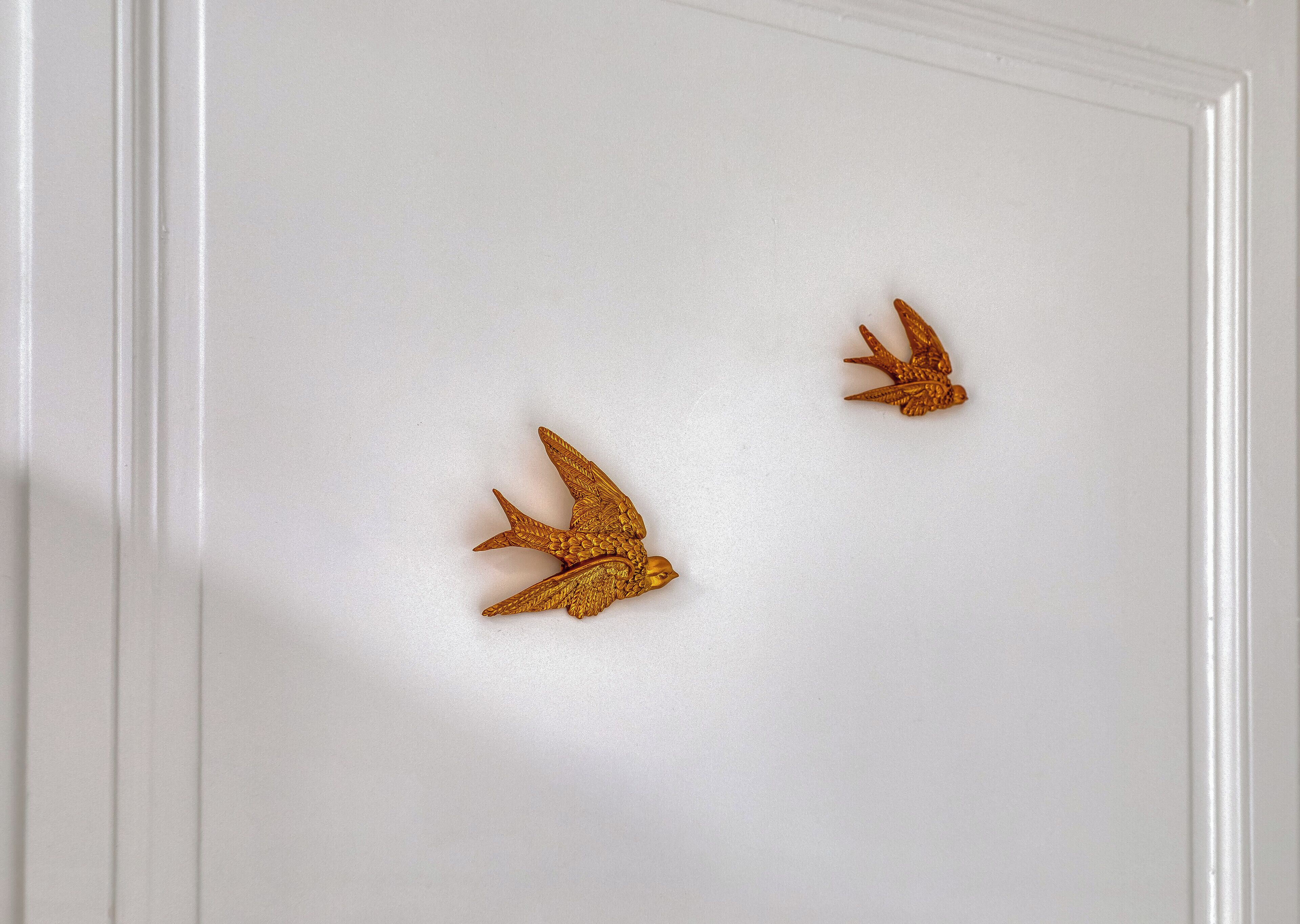 Eine weiße Tür mit zwei goldenen Vogelornamenten.