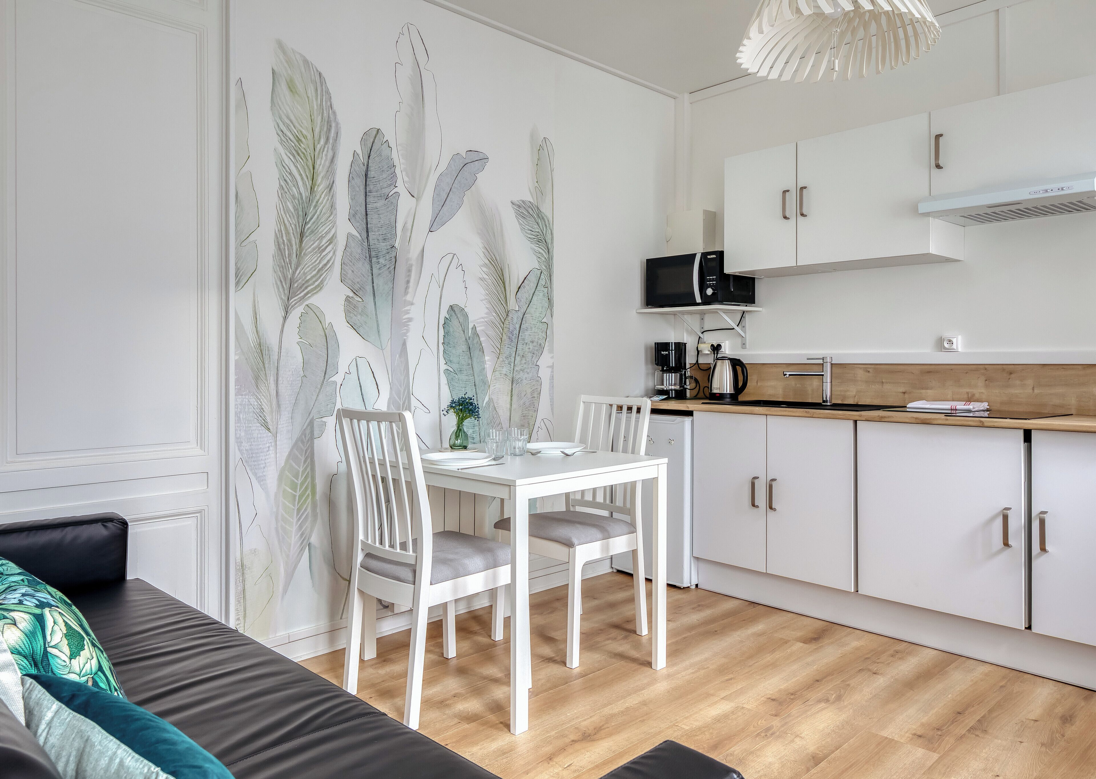 A modern kitchen with white cabinetry, a dining table with chairs, a microwave, and a coffee maker.