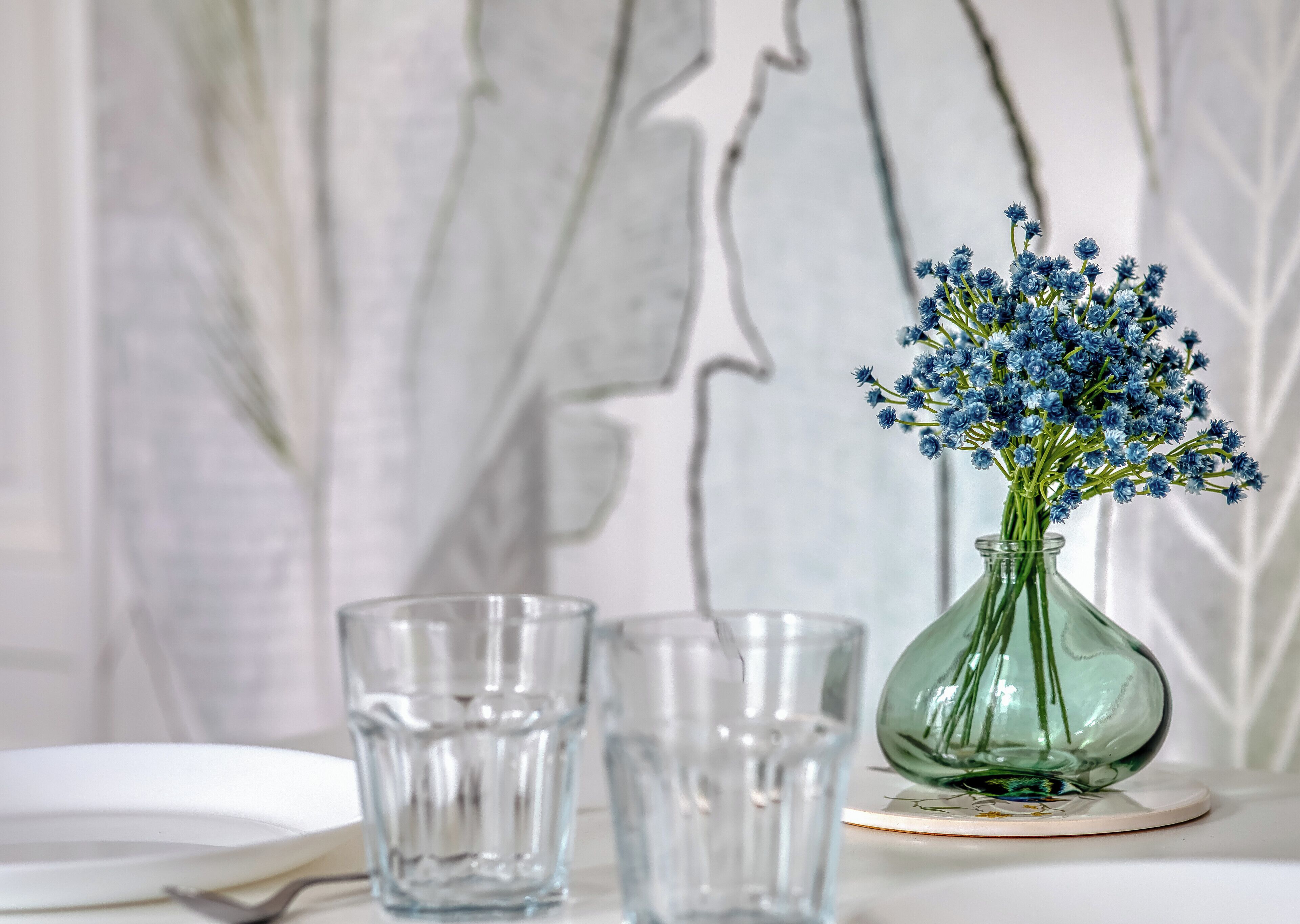 Eine klare Glasvase mit blauen Blumen auf einem weißen Tisch vor einer Marmorwand.