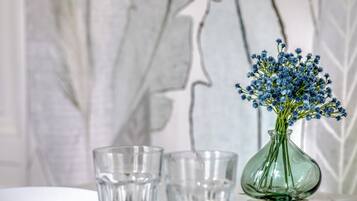 Eine klare Glasvase mit blauen Blumen auf einem weißen Tisch vor einer Marmorwand.