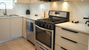 Une cuisine moderne dotée d’appareils électroménagers en acier inoxydable, de meubles en bois et d’une fenêtre avec des stores.