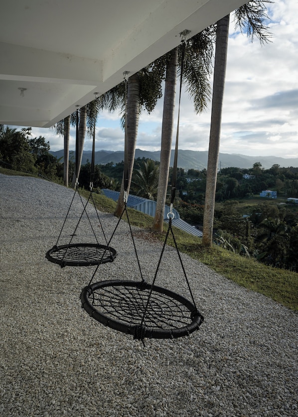 Two hanging circular wicker baskets under a white structure, with palm trees and a mountainous landscape in the background.