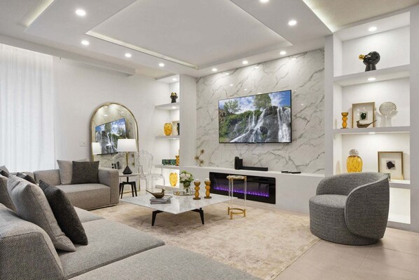 A modern living room with a fireplace, a large TV, and a marble wall. - Fun & Elegant w Pool, Cinema & Game Room (Davenport)