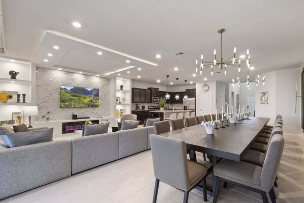 Una cocina moderna con armarios oscuros, una isla central y un comedor con una mesa larga y sillas.