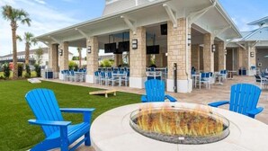Un patio al aire libre con sillas Adirondack azules, un hogar para fogata y una zona de estar cubierta con mesas y sillas.