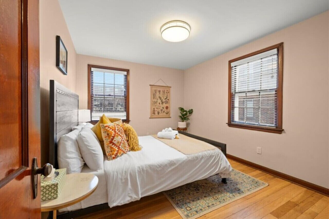 A bedroom with a bed, a bedside table, a window, and a ceiling light.