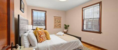 A bedroom with a bed, a bedside table, a window, and a ceiling light.