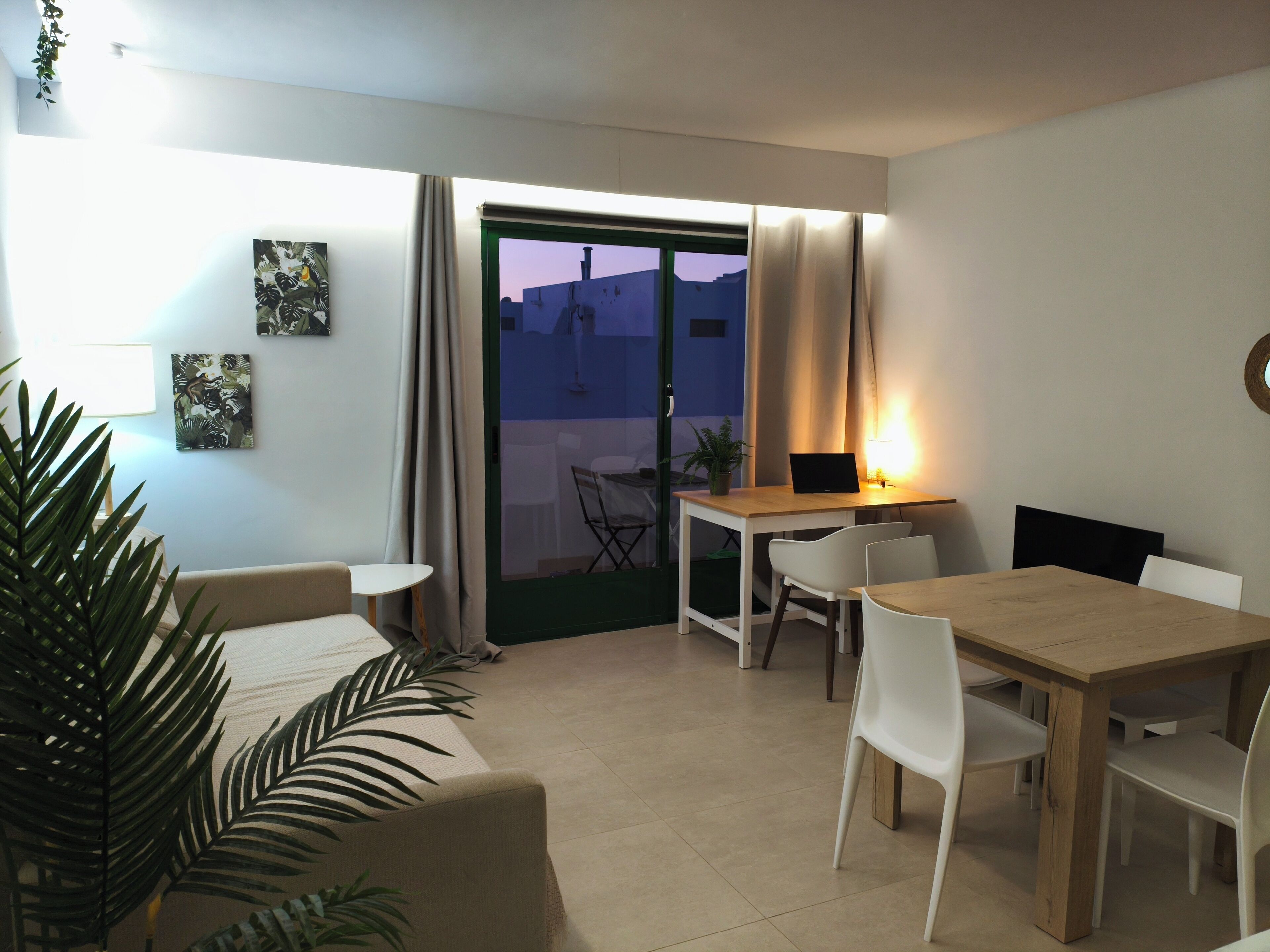 Een moderne woonkamer met een bank, een eettafel met stoelen, een laptop op tafel, en uitzicht door de glazen deur.