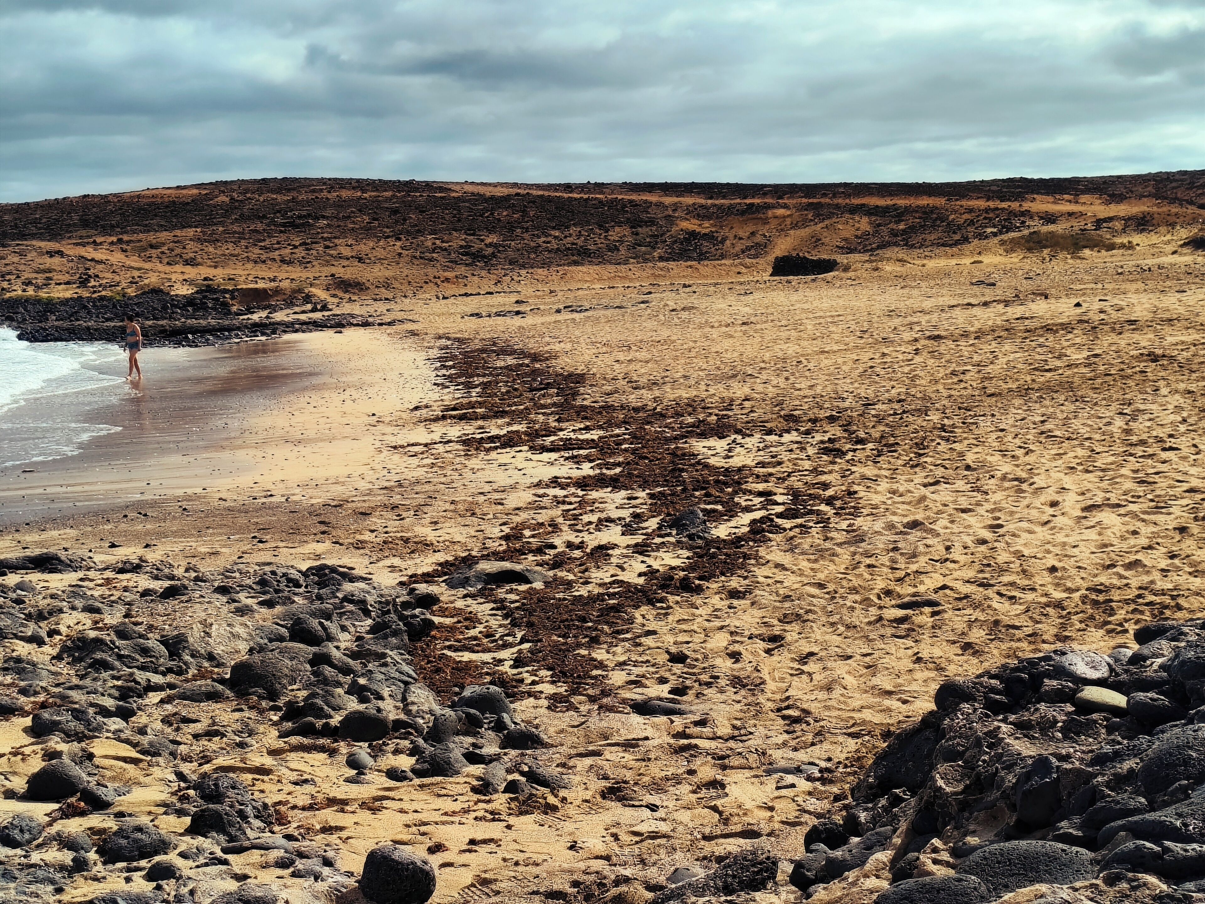 Een strand met rotsachtig terrein en schaarse begroeiing.
