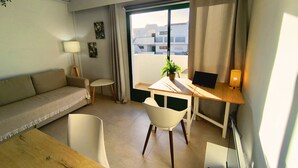 Moderni hotellihuone, jossa on sohva, pieni pöytä, kannettavalla tietokoneella varustettu työpöytä, tuoli ja ruukkukasvi.