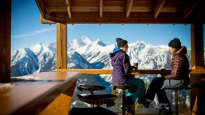 Dos personas sentadas en una mesa de madera con vistas a montañas nevadas.