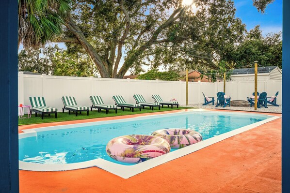 Ein Swimmingpool mit Liegestühlen und aufblasbaren Ringen, umgeben von einem weißen Zaun und Bäumen.