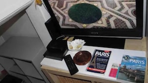 A television displaying a patterned floor, a remote control, a book titled 'Paris', and a small bowl on a table. - Beau Studio Rue Didot (Paris)