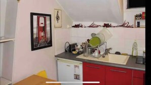 A kitchen with a sink, a dish rack, and a refrigerator. There are red cabinets and a white countertop. - Beau Studio Rue Didot (Paris)