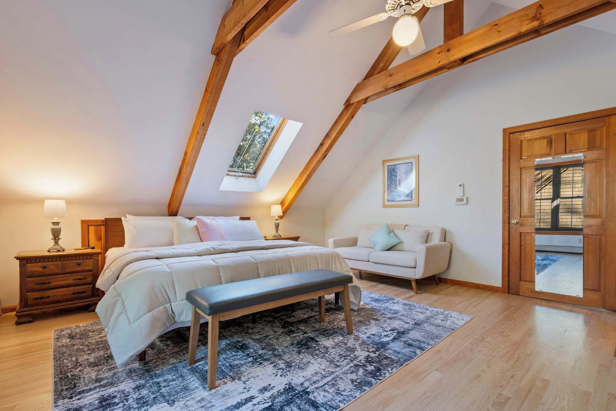 Een slaapkamer met een schuine hemel, een bed, een bankje, een nachtkastje, een lamp, een raam en een deur.