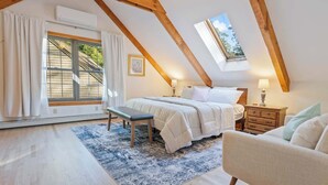 Et soveværelse med skråvæg, en seng, en bænk, et kommode og et vindue med udsigt ud