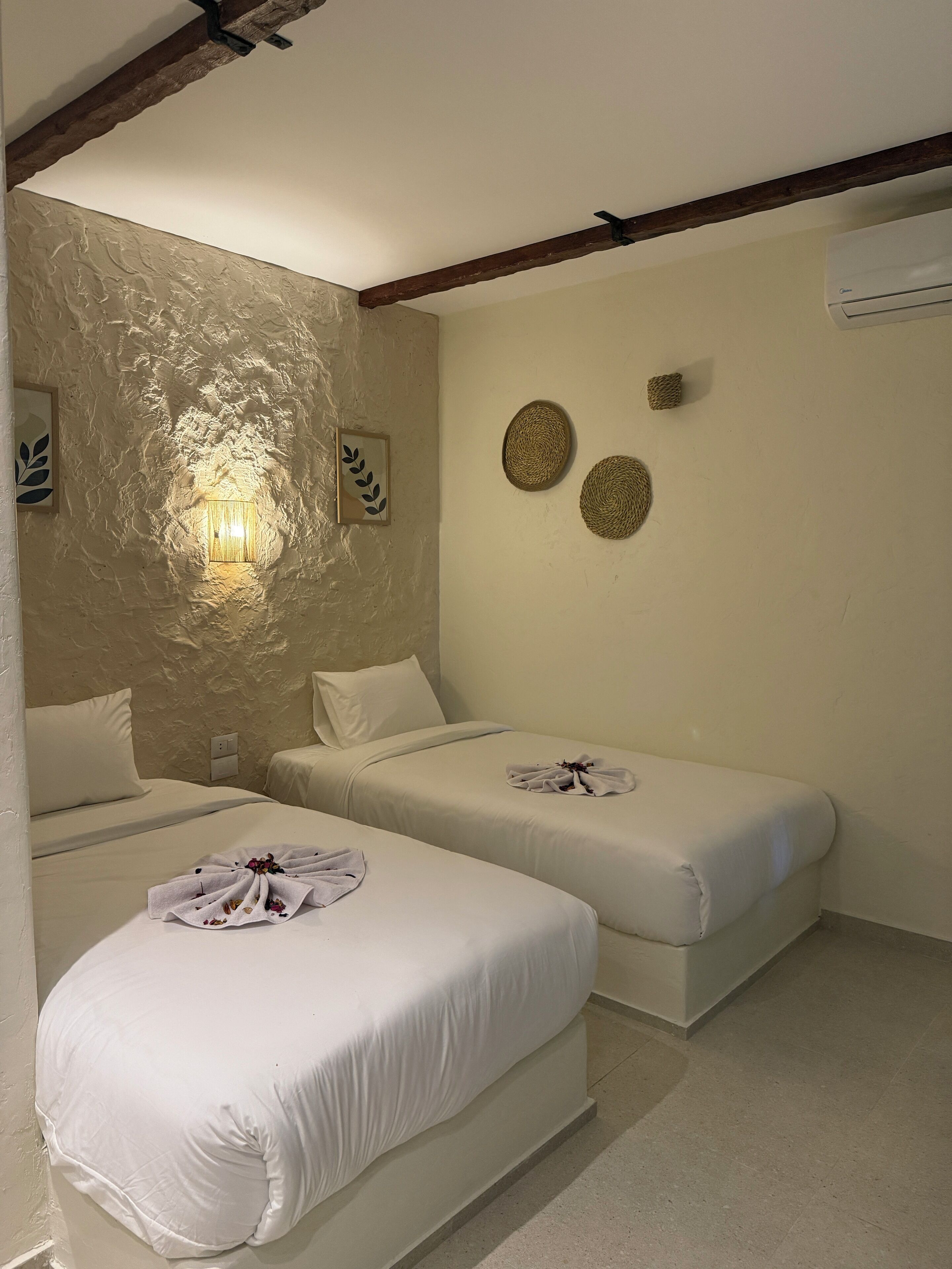 A room with two beds, a textured wall, a wall-mounted air conditioner, and two wall-mounted decorative items.