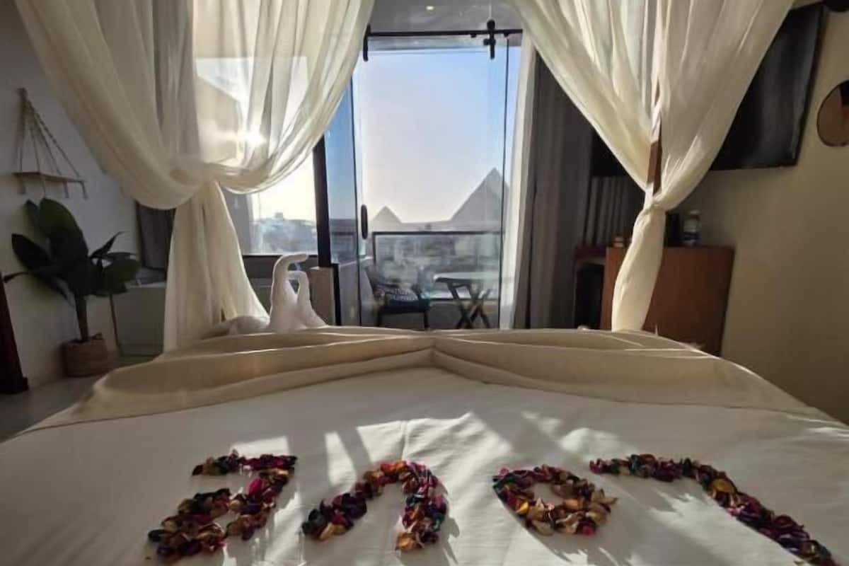 A bed with a view of the pyramids, a balcony, and a plant.