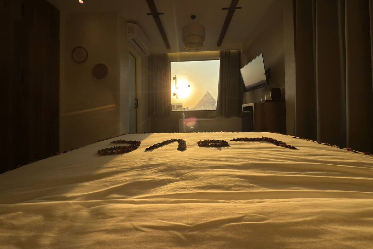 A hotel room with a bed, a television, and a view of a pyramid.