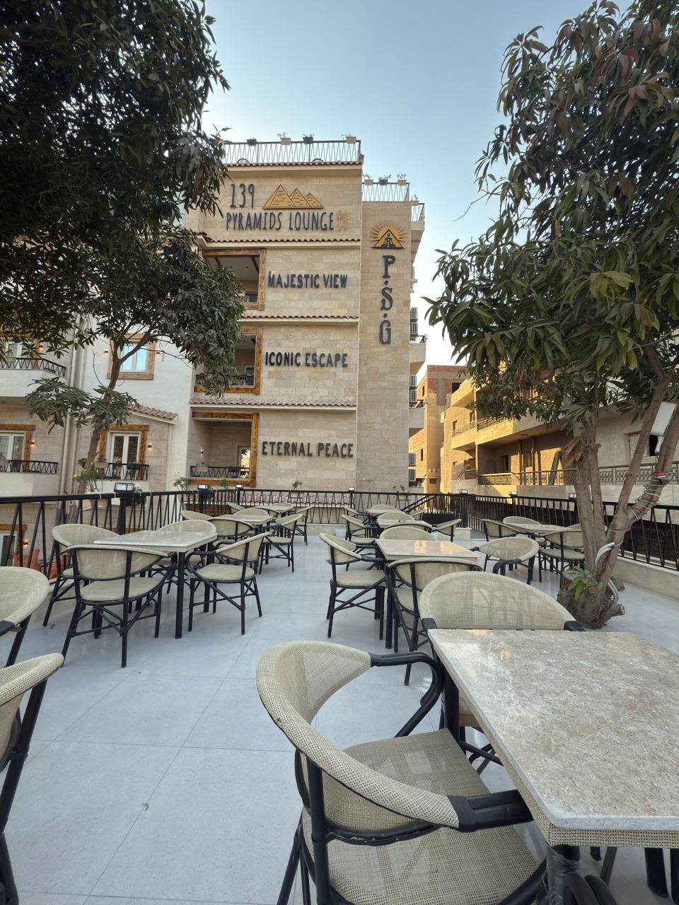 Un área de lounge en la azotea con asientos al aire libre y un edificio con letreros que indican nombres como "139 Pyramids Lounge", "Majestic View", "Iconic Escape" y "Eternal Peace".