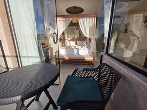 A balcony with a table and chairs, a bed with white bedding, and a glass door leading to the room. - Pyramids Spiritual Gate (Giza)