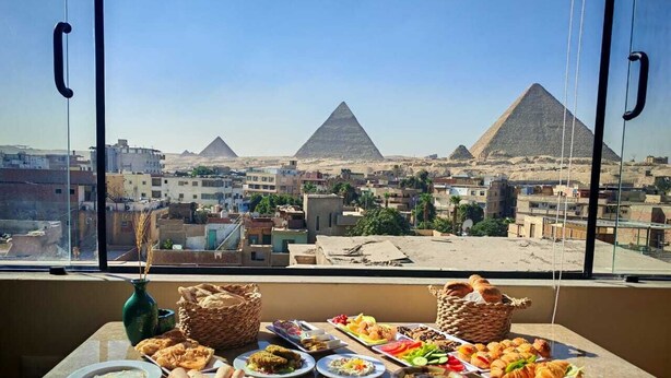 A dining table with various dishes and a view of the pyramids. - Pyramids Spiritual Gate  (Giza)