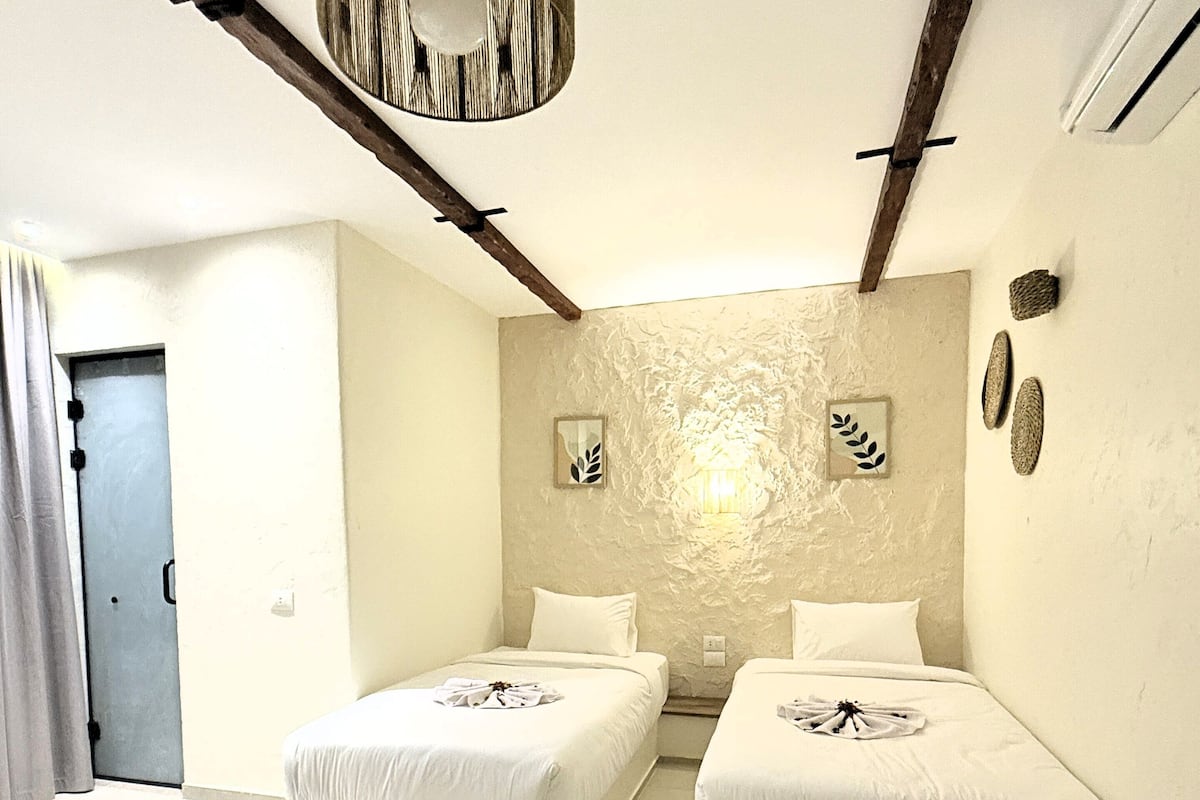 A modern bedroom with two beds, a wooden ceiling beam, a textured wall, and a hanging light fixture.