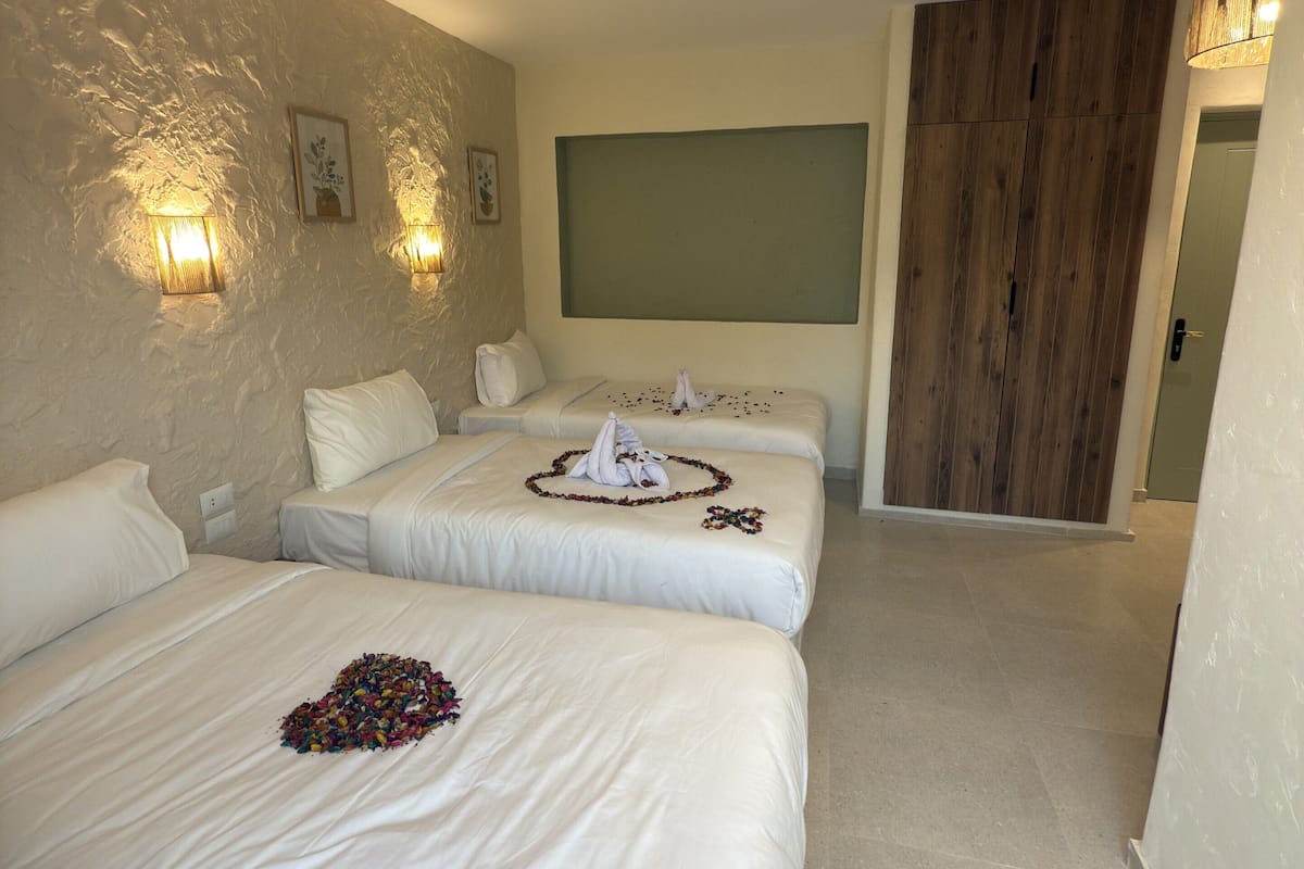A hotel room with two beds, a wooden ceiling beam, a green panel, and a wooden door.