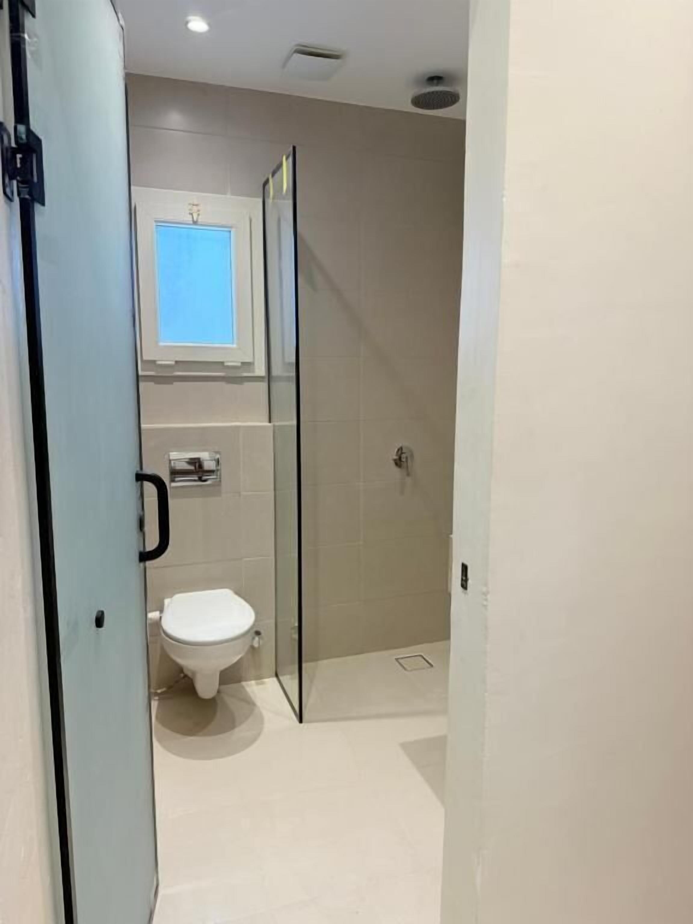 A bathroom with a toilet, a glass shower enclosure, and a window above the toilet.