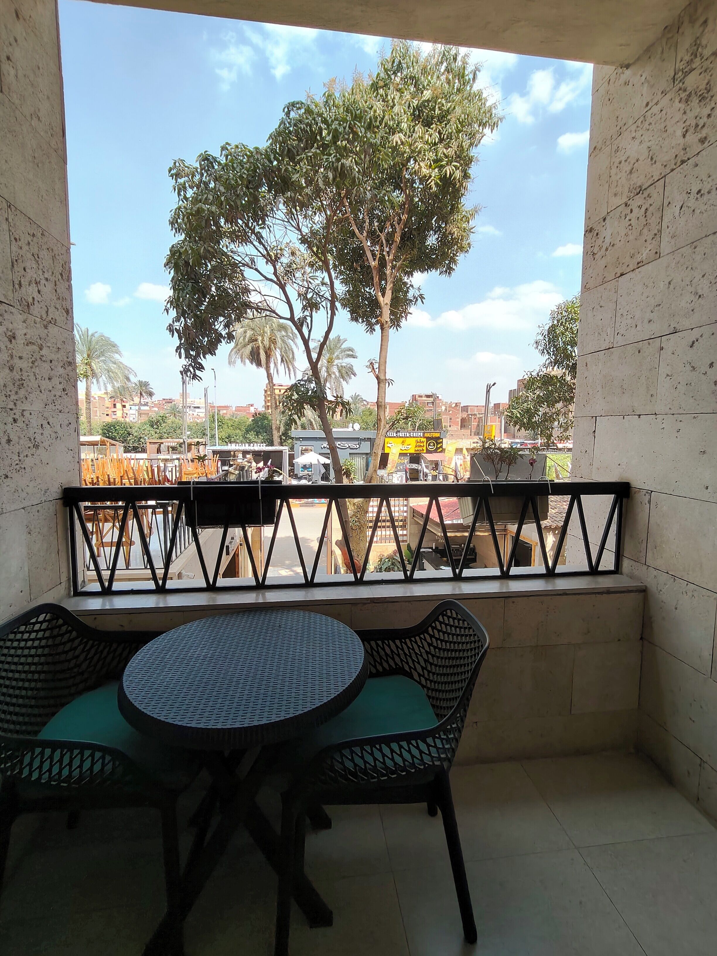 A balcony with a table and chairs, a view of a tree, and a street with buildings and vehicles.