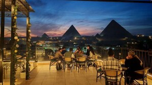 A terrace with tables and chairs, overlooking pyramids at dusk. - Pyramids Spiritual Gate  (Giza)